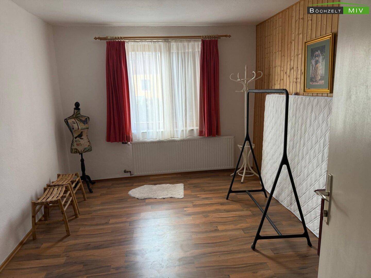 Schlafzimmer mit Holzboden, Holzpaneelen an einer Wand und einem großen Fenster.