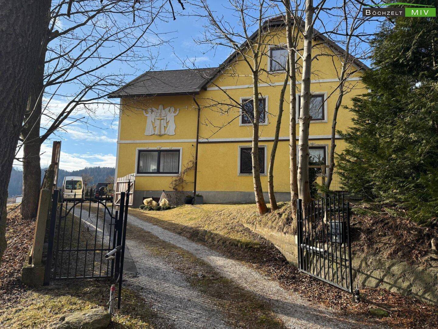 Gelbes Haus mit Einfahrt, umgeben von Bäumen und einem gepflegten Vorgarten.