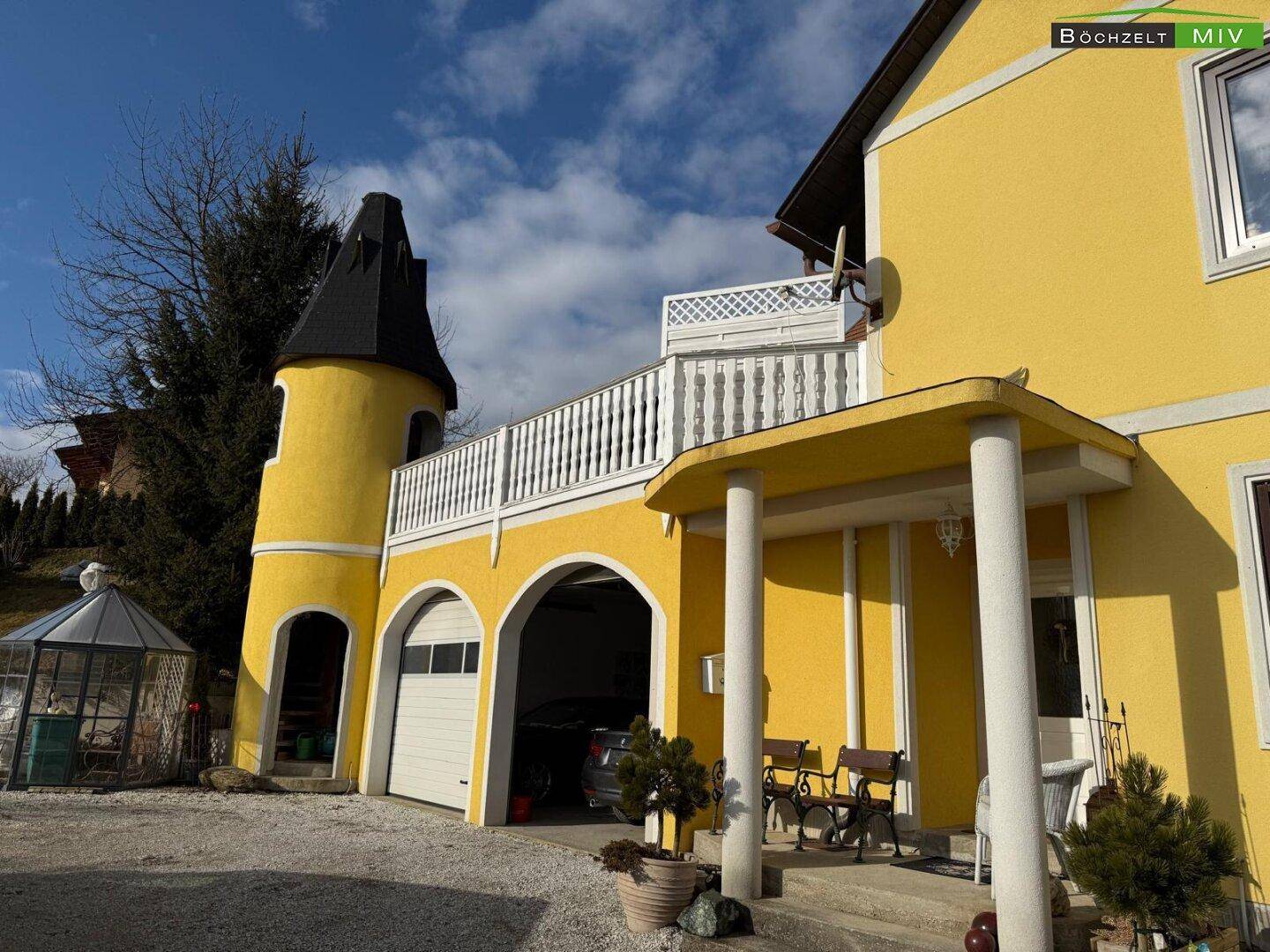 Gelbe Fassade eines Hauses mit Turm, Garage und überdachtem Eingangsbereich.