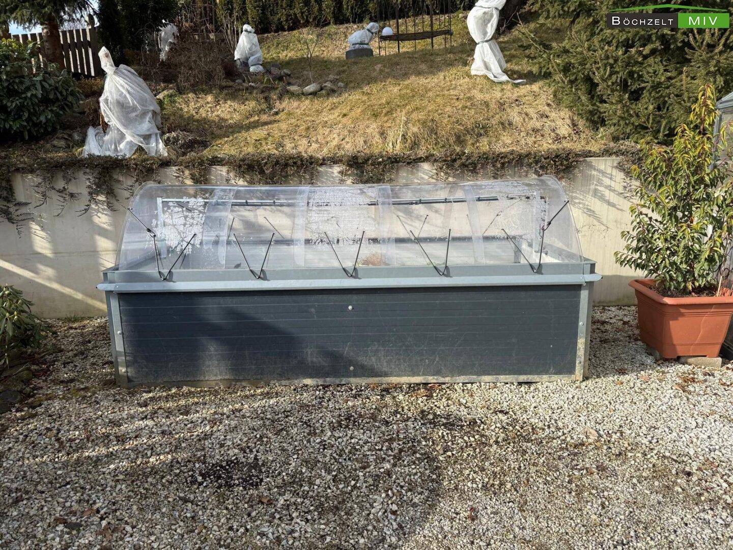 Kleines Gewächshaus oder Frühbeet im Gartenbereich, umgeben von Kies.