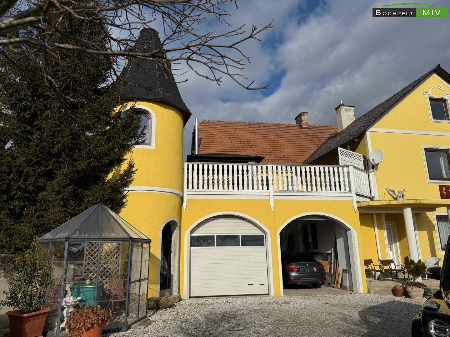 Gelbes Haus mit Turm, Garage und einem kleinen Gewächshaus im Vorgarten.