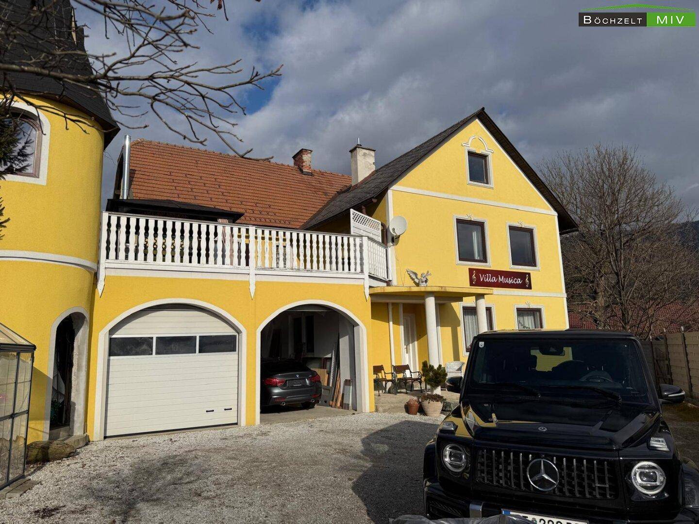 Gelbes Haus mit Turm, Garage und einem geparkten schwarzen Geländewagen davor.