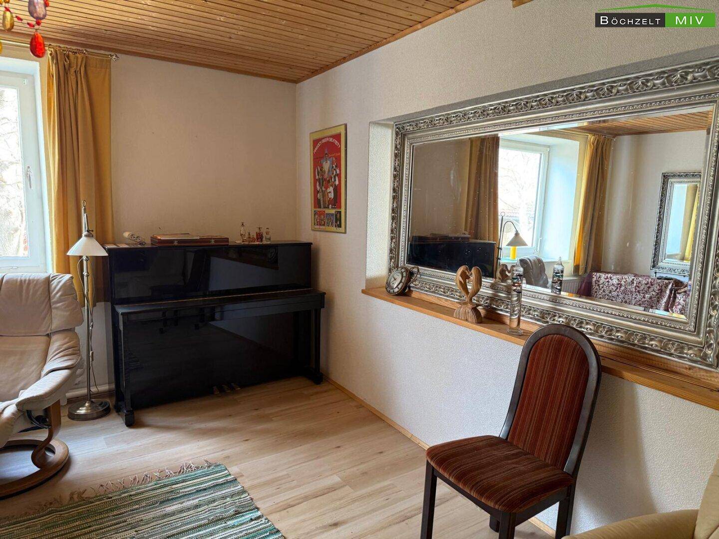 Helles Wohnzimmer mit Holzboden, großem Spiegel und einem Klavier.