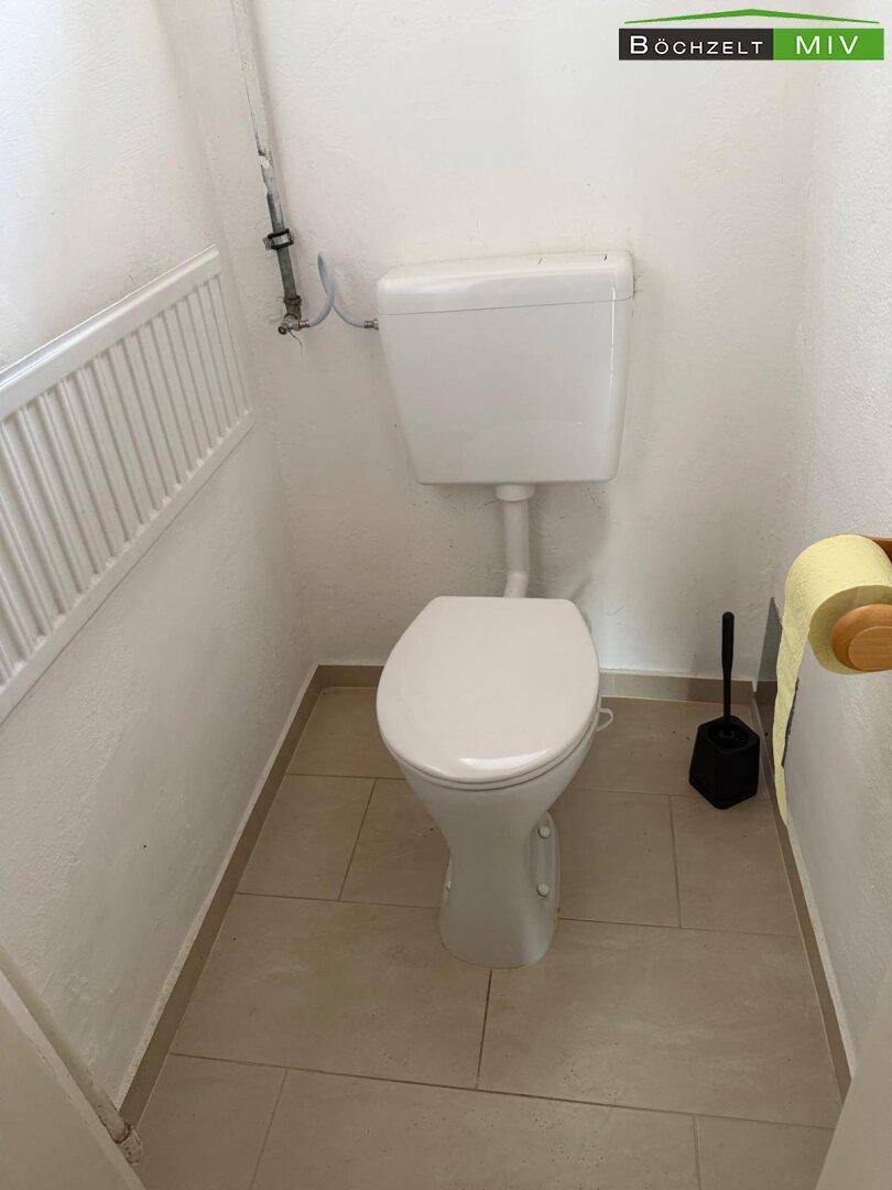 Kleines WC mit Toilette, Fliesenboden und Heizkörper an der Wand.