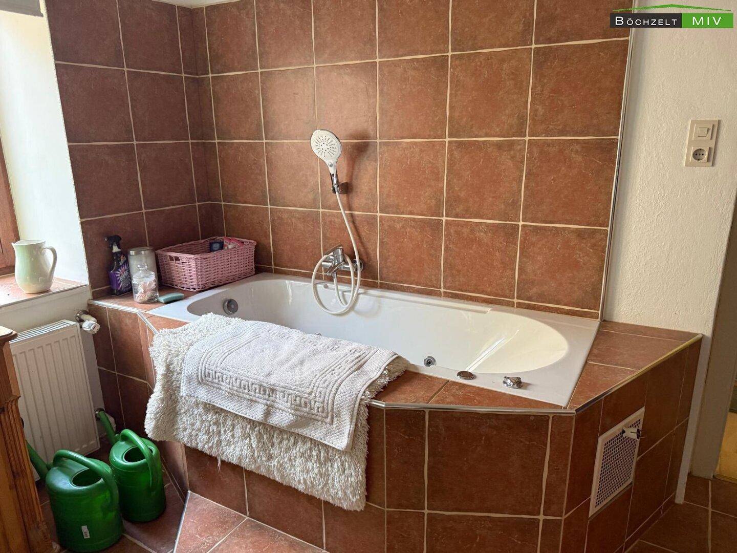 Badezimmer mit eingebauter Eckbadewanne, Duschbrause und braunen Fliesen im 80er-Jahre-Stil.
