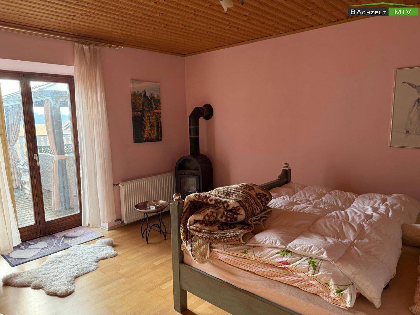 Gemütliches Schlafzimmer mit Holzbalkendecke, rosa Wänden, Kaminofen und direktem Zugang zum Balkon.