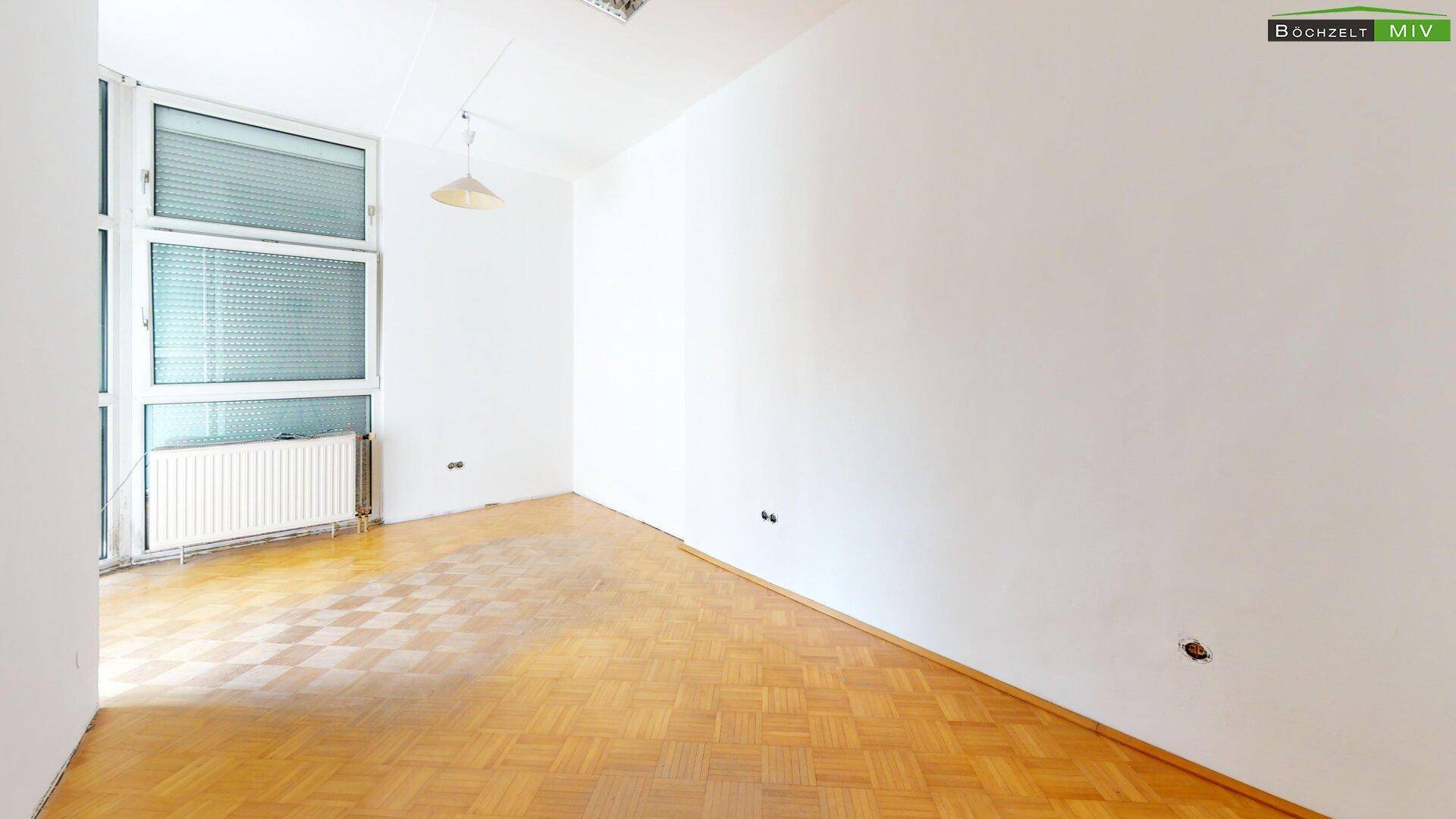 Helles Zimmer mit Parkettboden und großem Fenster, bietet viel Tageslicht und eine angenehme Atmosphäre.