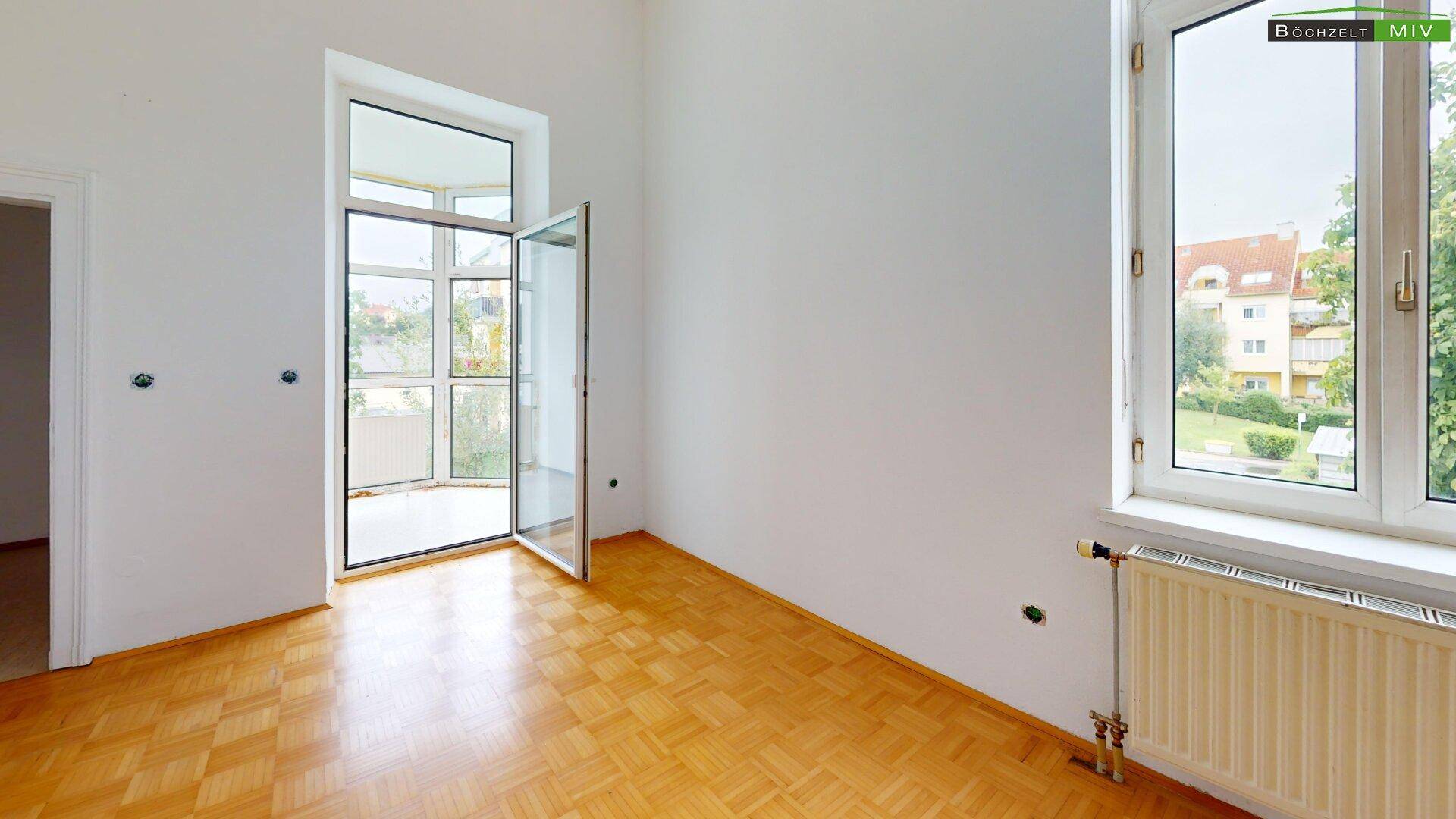 Geräumiges Zimmer mit großen Fenstern und Parkettboden, bietet viel Tageslicht und Blick ins Grüne.