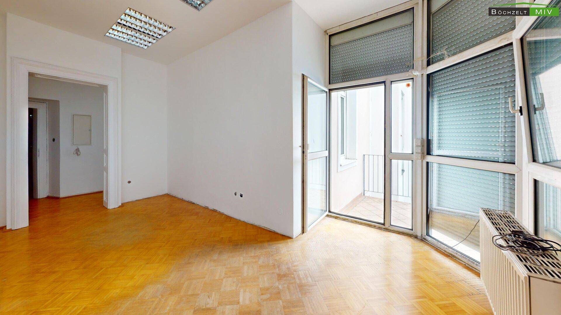 Heller Raum mit Parkettboden und Zugang zu einem Balkon, ausgestattet mit Rollläden für Privatsphäre.