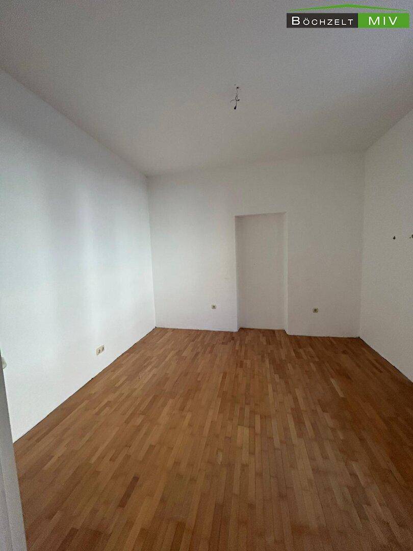 Leeres Schlafzimmer mit hellem Holzboden und weißen Wänden, bereit zur individuellen Gestaltung.