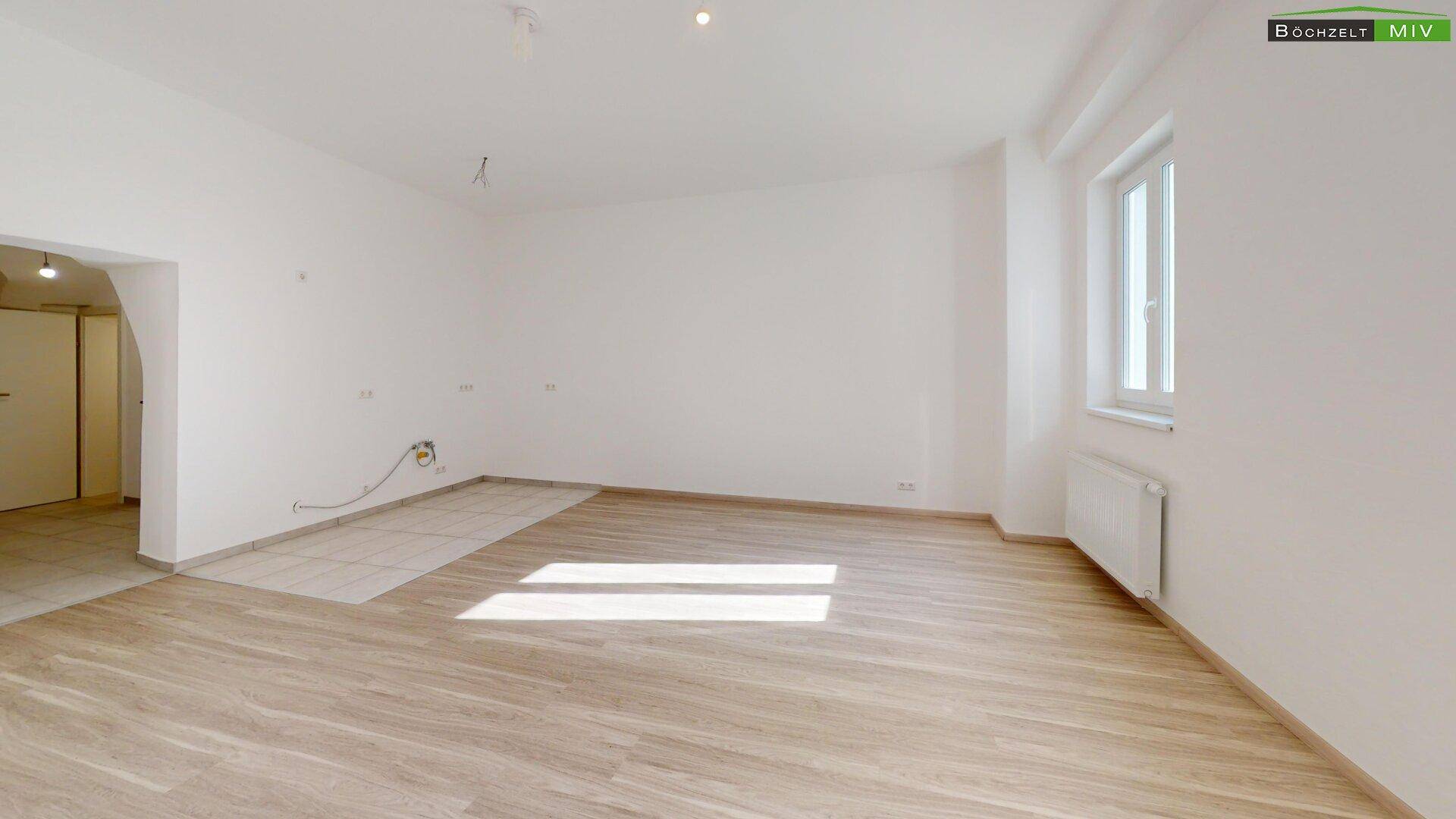 Heller Raum mit Laminatboden und Fliesenbereich, vorbereitet für eine Küche mit Anschlussmöglichkeiten.