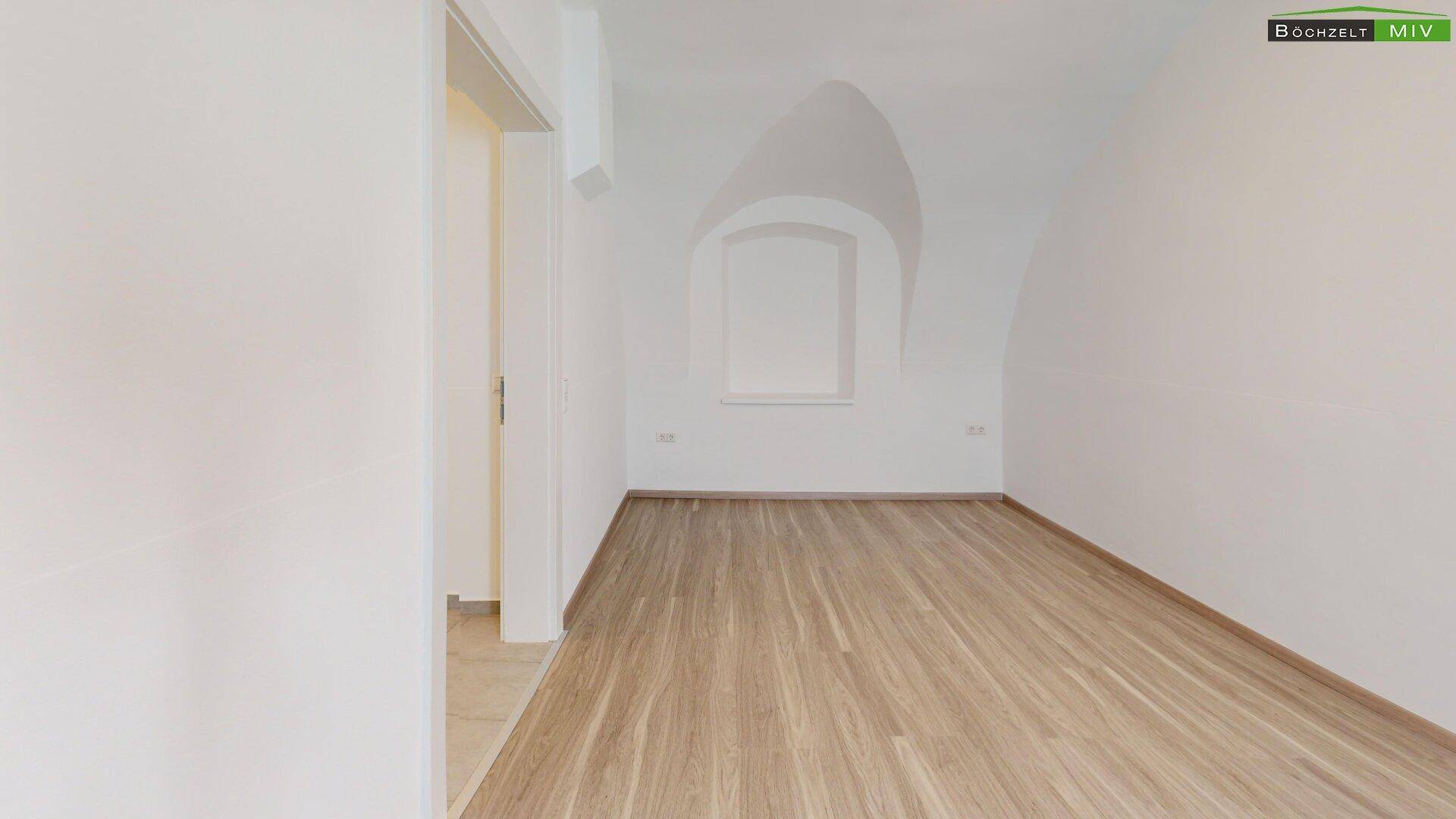 Leerer Raum mit Laminatboden, weiß gestrichenen Wänden und einer dekorativen Nische mit Gewölbedecke.