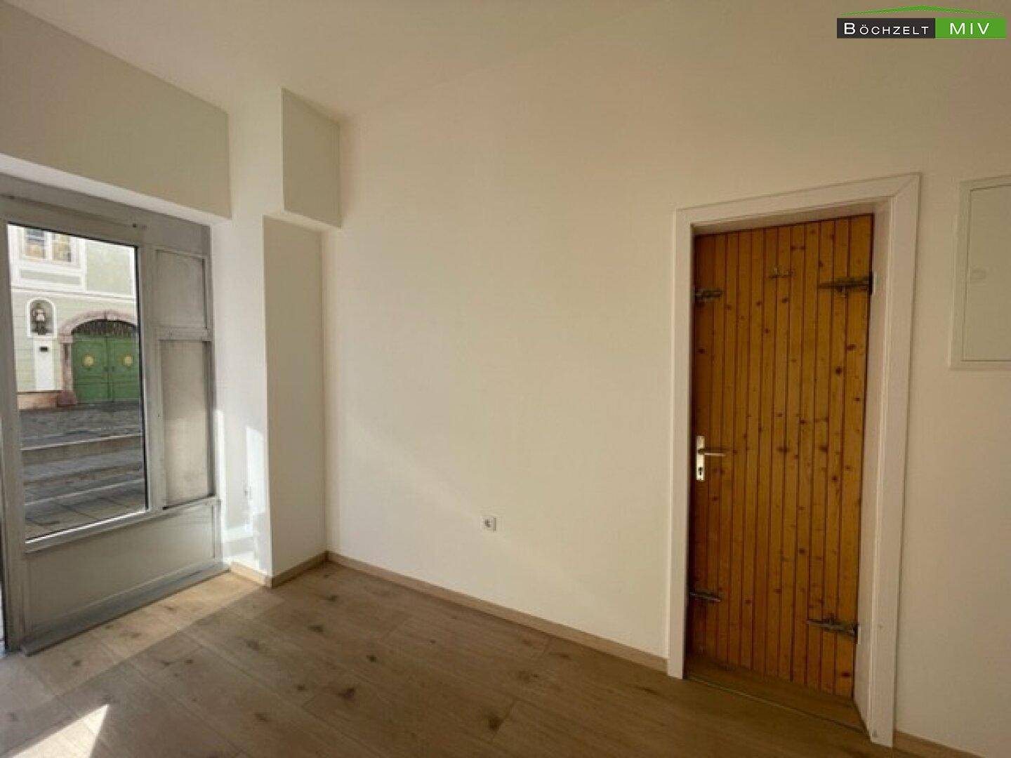 Leerer Raum mit hellem Holzboden, weiß gestrichenen Wänden und einer rustikalen Holztür.