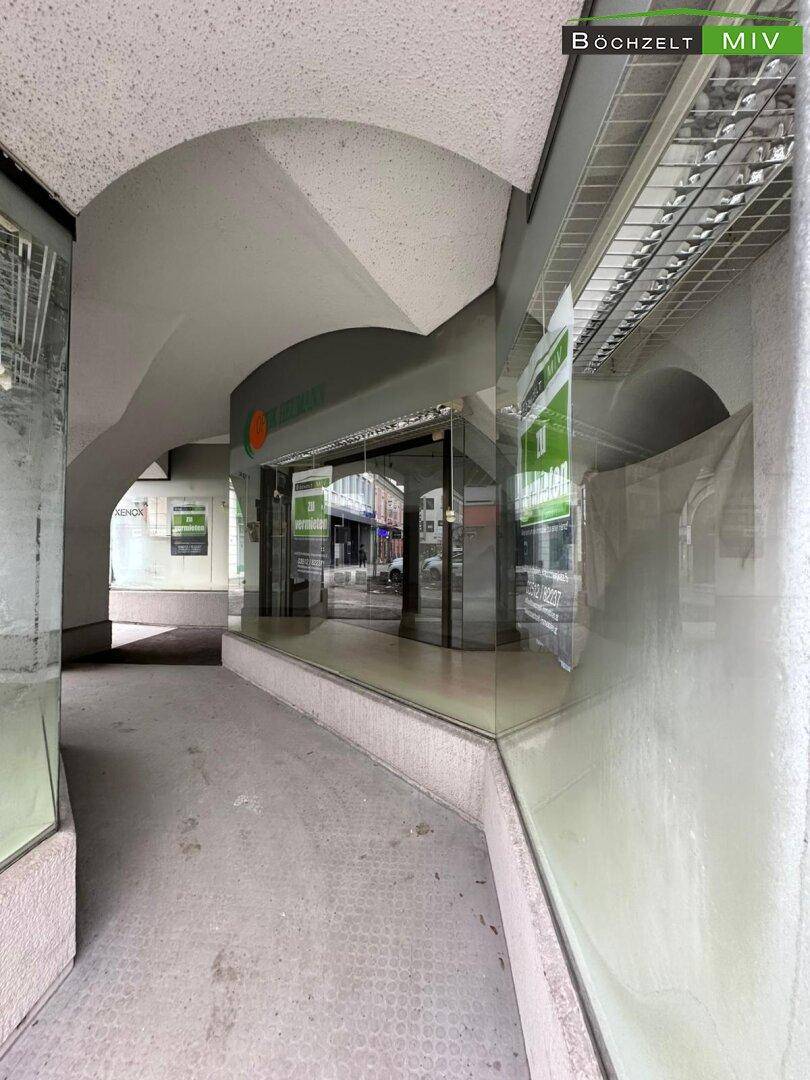 Ansicht der Ladenfront mit großen Glasfenstern und einem überdachten Eingangsbereich, der eine Passage bildet.