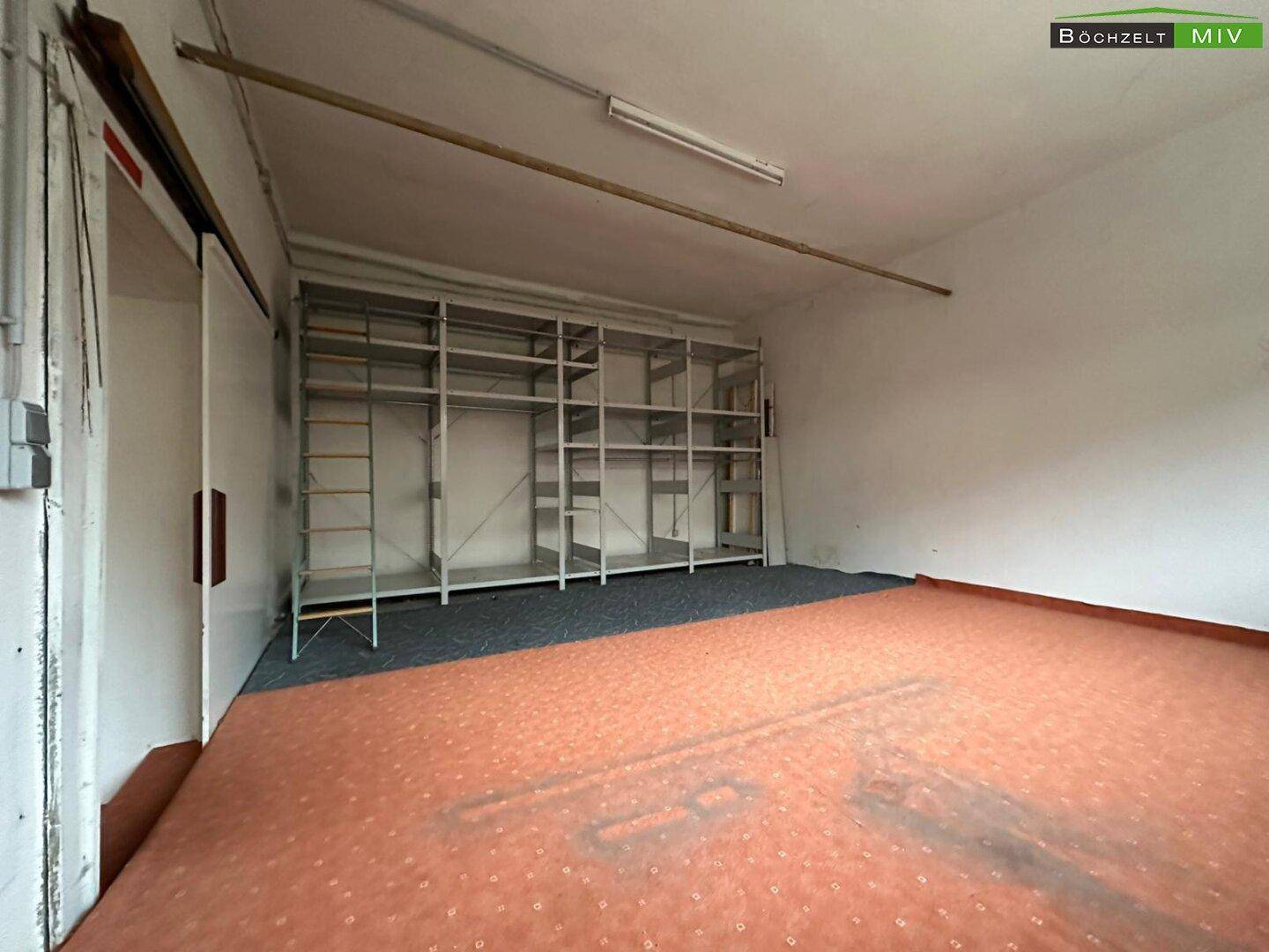Lagerraum mit Teppichboden, einfachen Regalen an der Wand und einer Schiebetür.