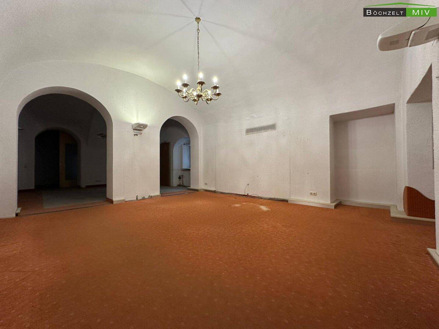 Geräumiger Gewerberaum mit gewölbter Decke, Teppichboden und dekorativen Wandleuchten.