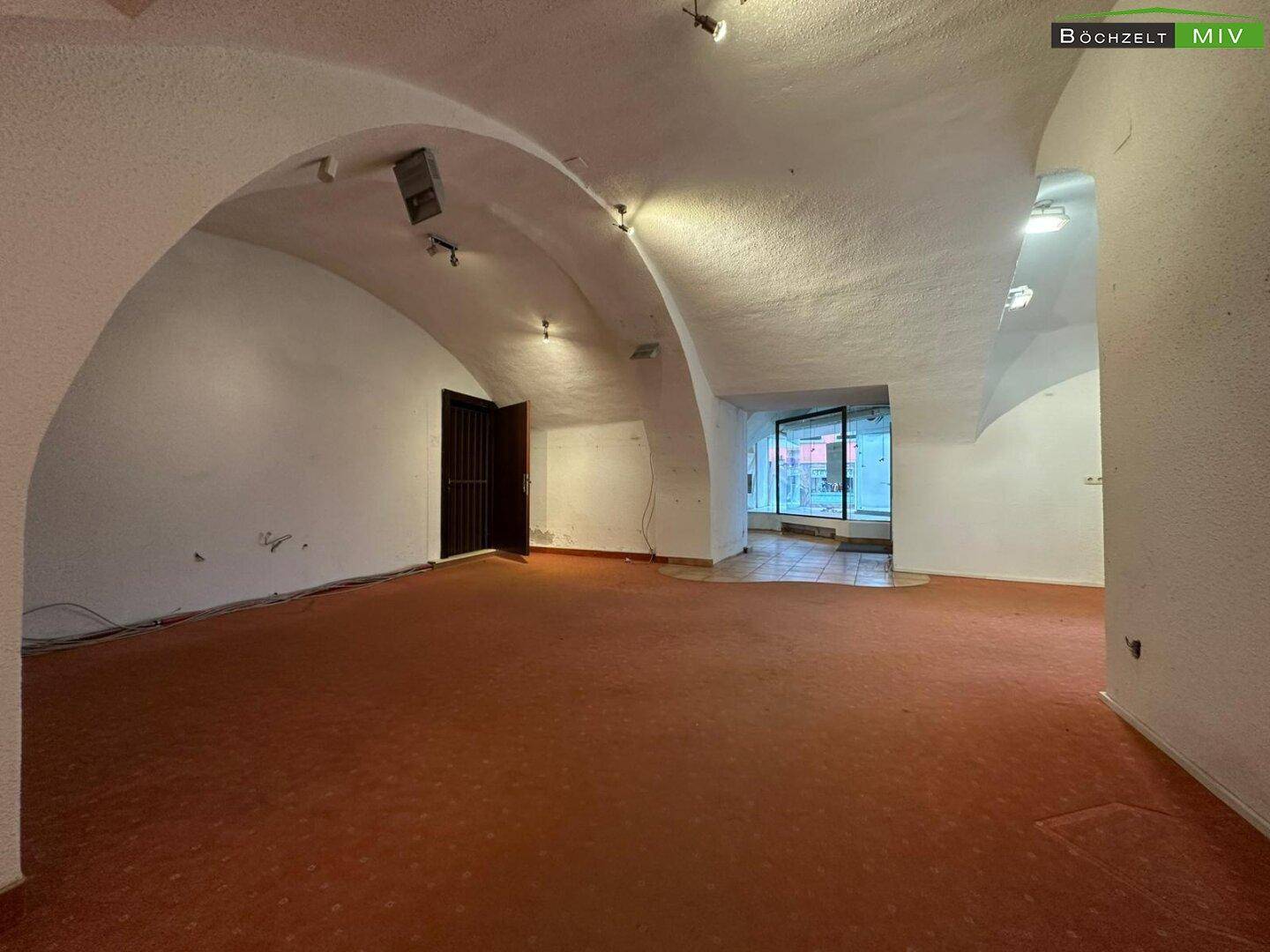 Offener Gewerberaum mit Teppichboden, gewölbter Decke und Blick auf die Schaufensterfront.