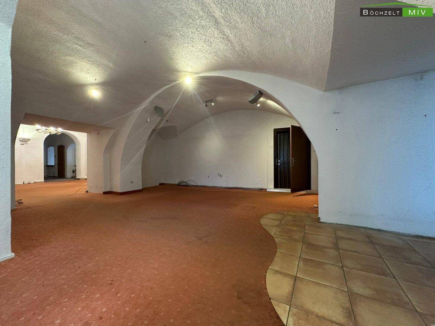 Geräumiger Gewerberaum mit Teppich- und Fliesenboden, gewölbter Decke und Blick auf den Eingangsbereich.