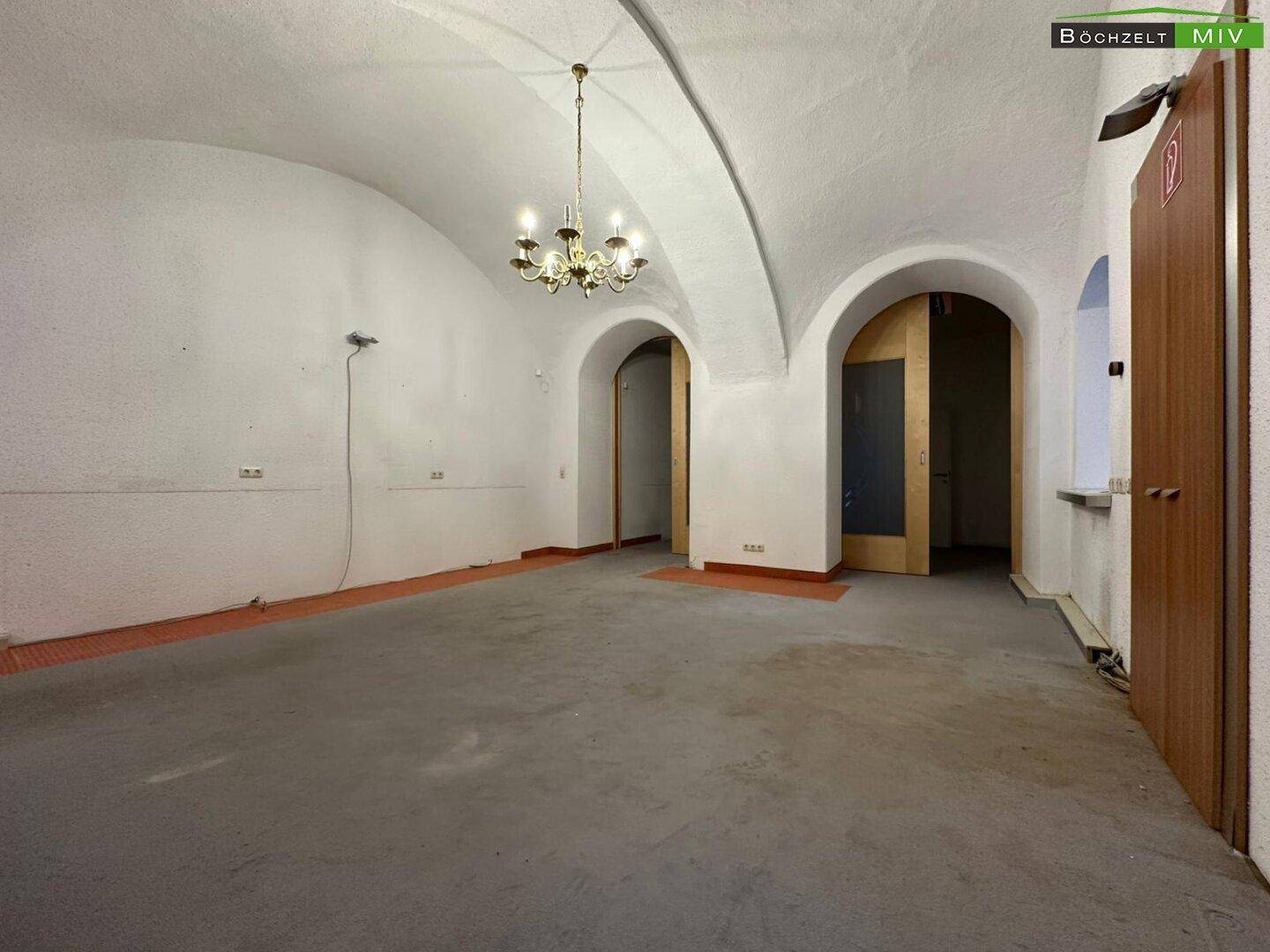 Großer Gewerberaum mit gewölbter Decke, Betonboden und einem Kronleuchter, der den Raum beleuchtet.