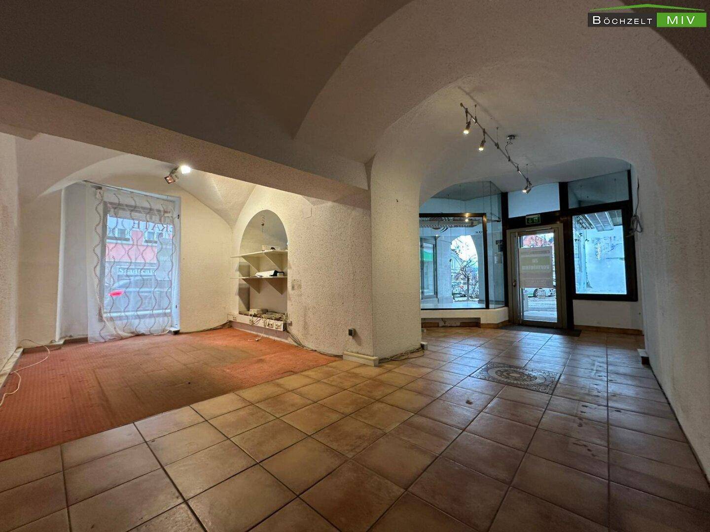 Hauptverkaufsfläche mit Fliesen- und Teppichboden, gewölbter Decke und Blick auf die großen Schaufenster.