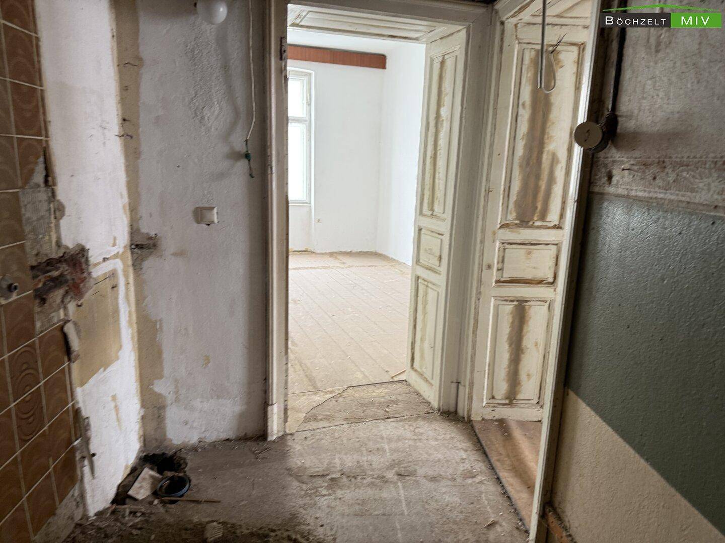 Renovierungsbedürftiger Raum mit alten Fliesen und abgenutzten Holztüren, bereit zur Sanierung.