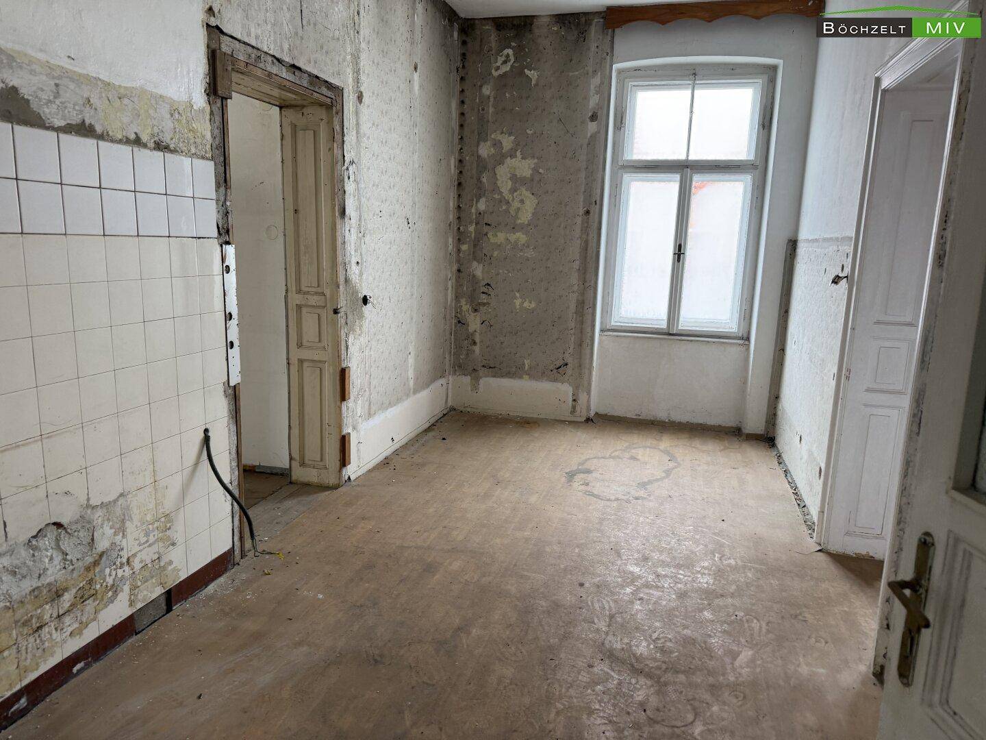Großer, renovierungsbedürftiger Raum mit alten Fliesen und einem Fenster, das Licht hereinlässt.