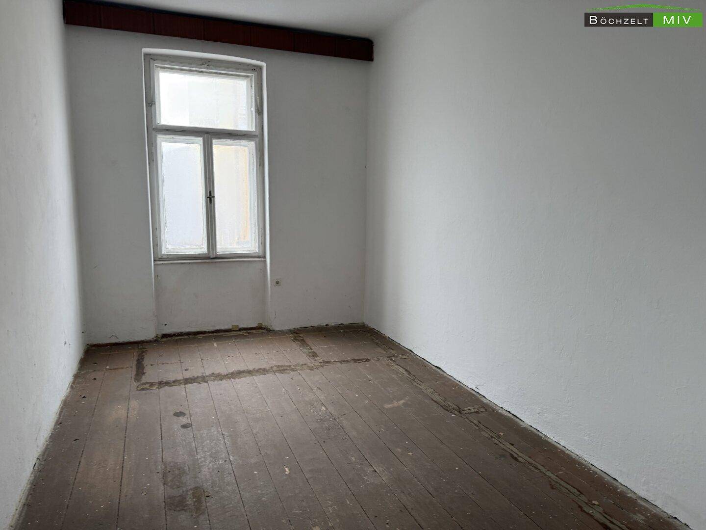 Leerer Raum mit altem Holzdielenboden und einem Fenster, das Tageslicht spendet.