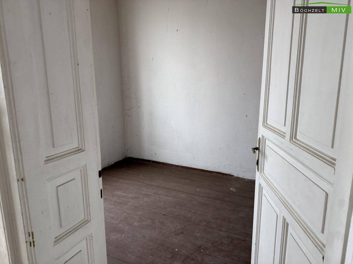 Blick durch eine alte Holztür in einen leeren Raum mit dunklem Holzdielenboden.