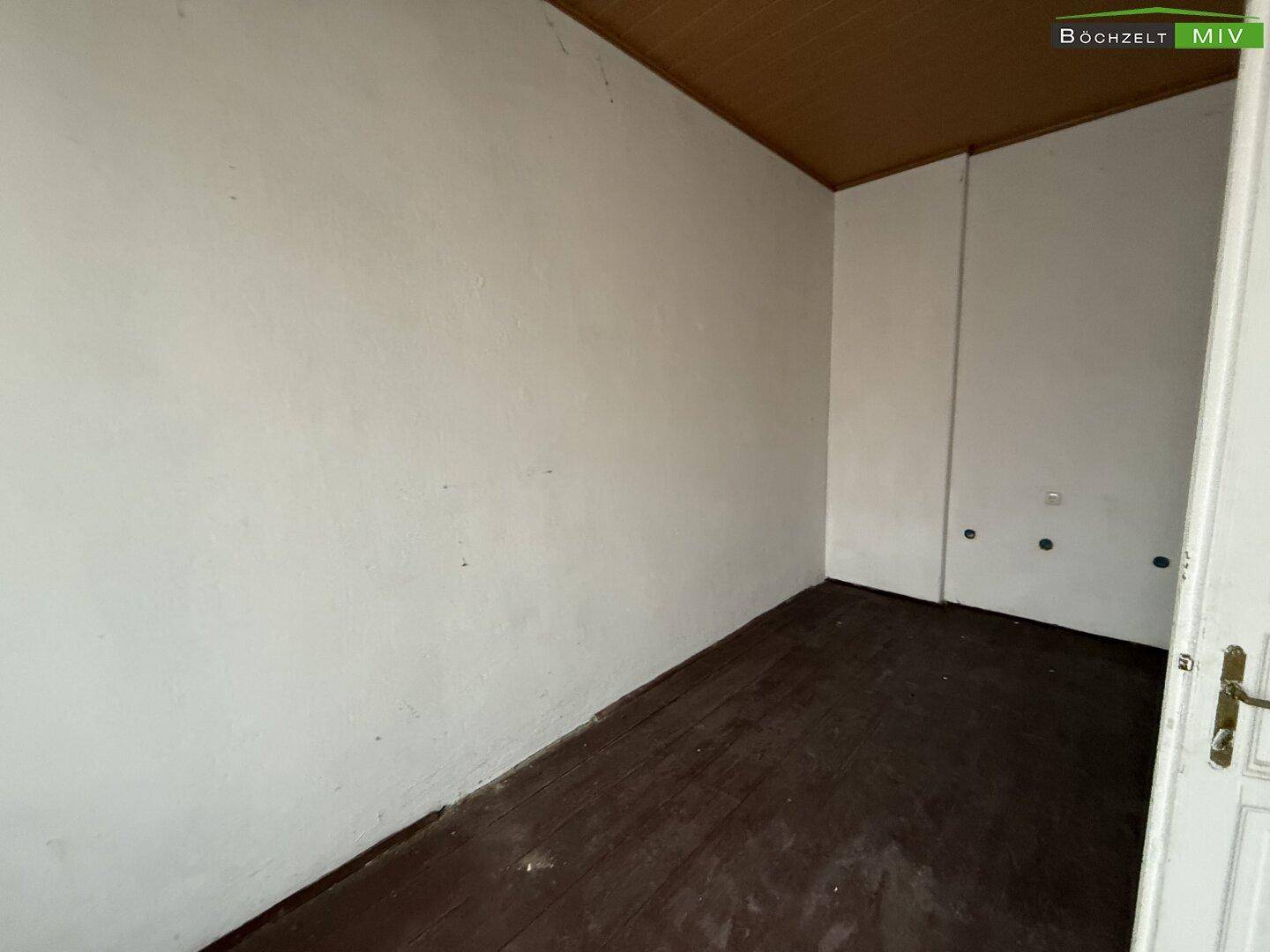 Kleiner, leerer Raum mit dunklem Holzdielenboden und einer Holzdecke, bereit zur Renovierung.