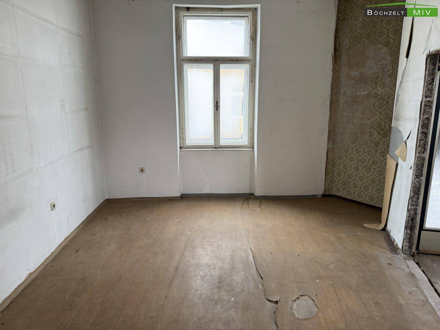 Renovierungsbedürftiger Raum mit altem Holzboden und einem Fenster, das Tageslicht hereinlässt.