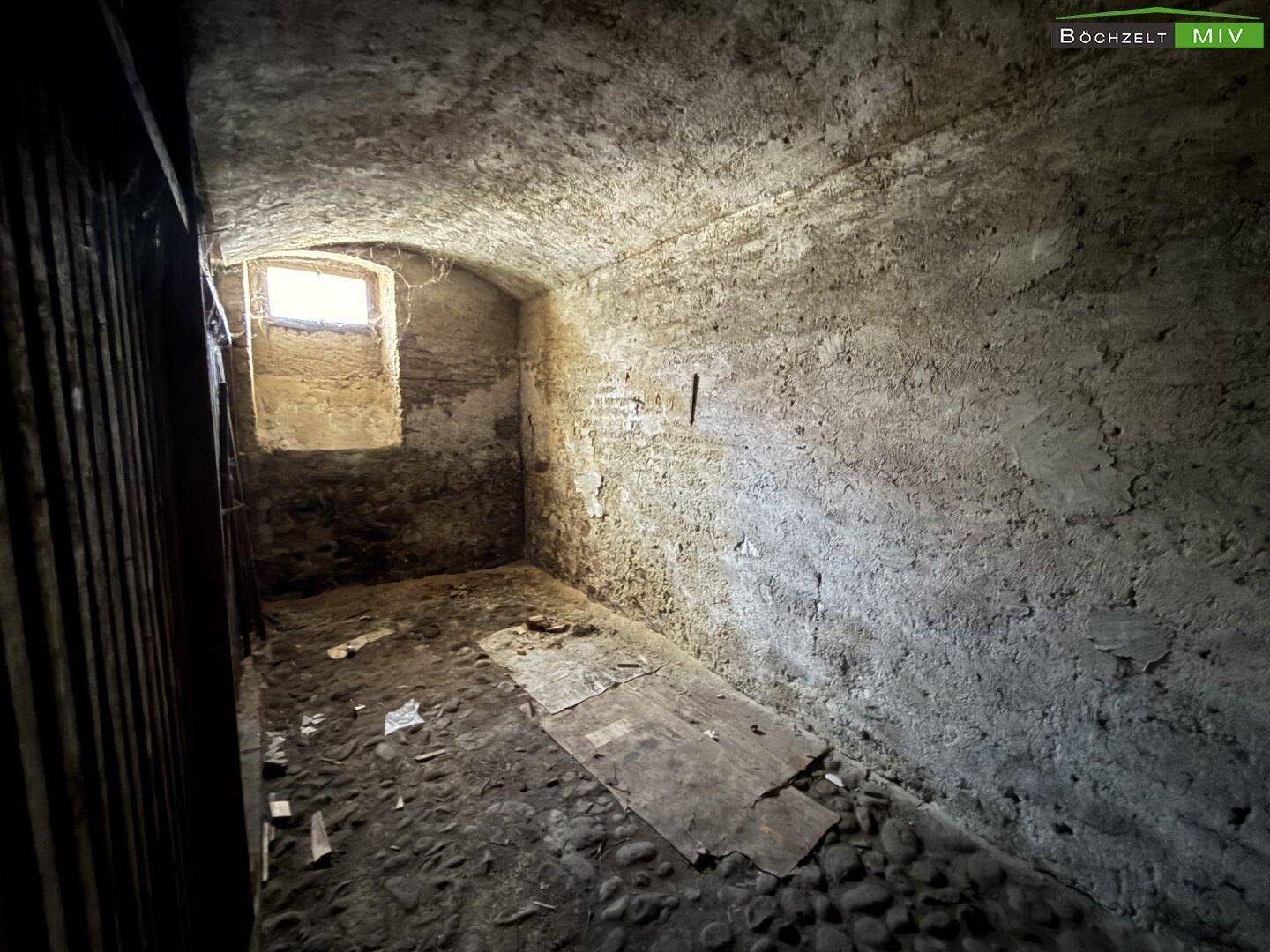 Dunkler Gewölbekeller mit rauen Steinwänden und einem kleinen Fenster, das Licht hereinlässt.