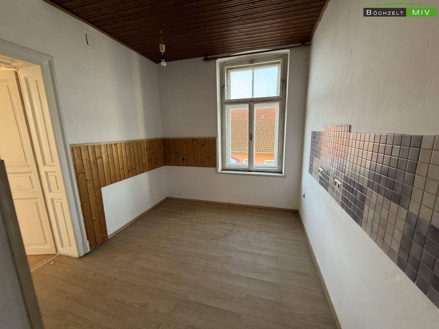 Renovierter Raum mit Laminatboden, Holzvertäfelung und einem Fenster mit Blick nach draußen.