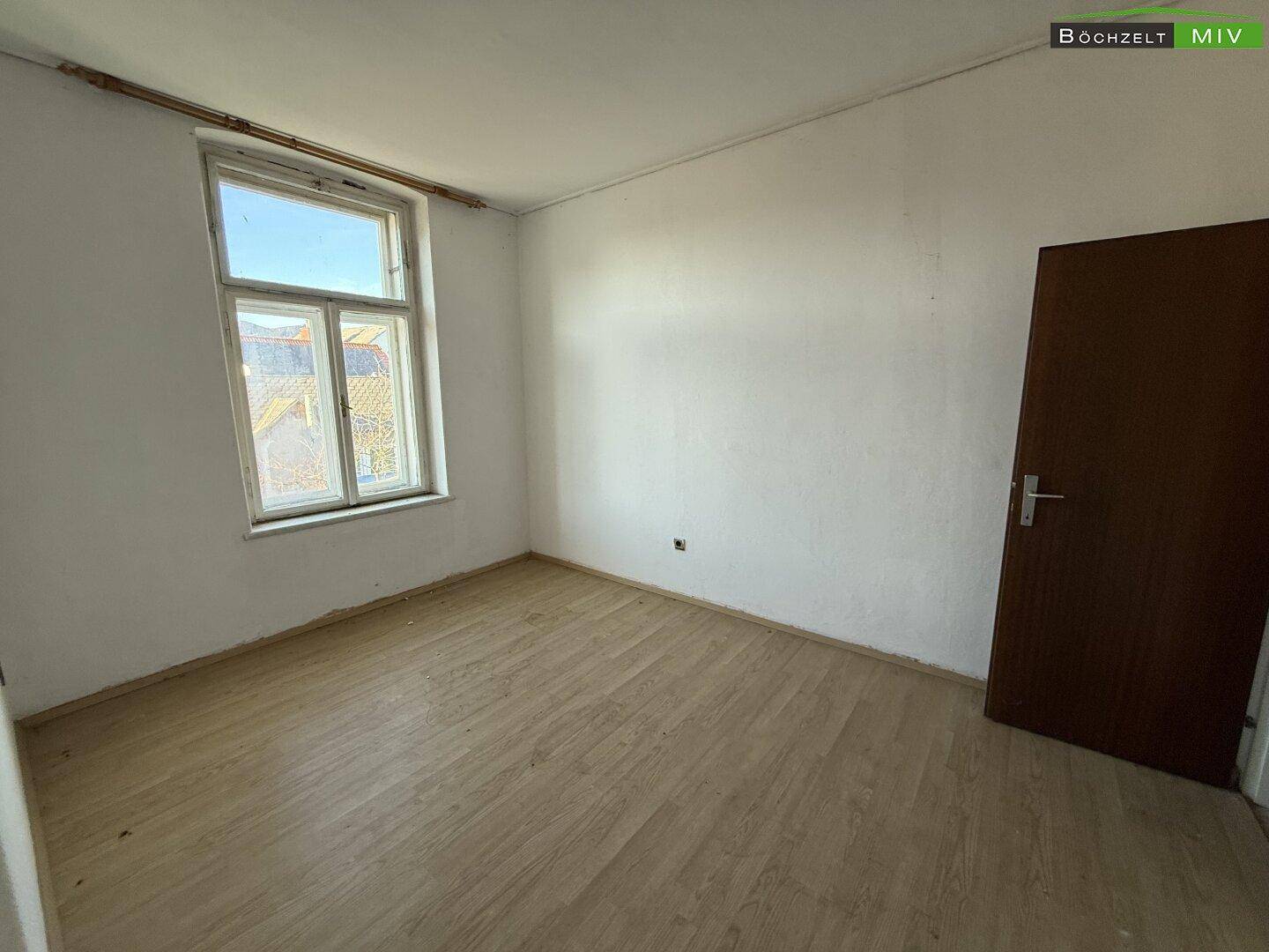 Heller Raum mit Laminatboden und einem großen Fenster, das viel Tageslicht hereinlässt.