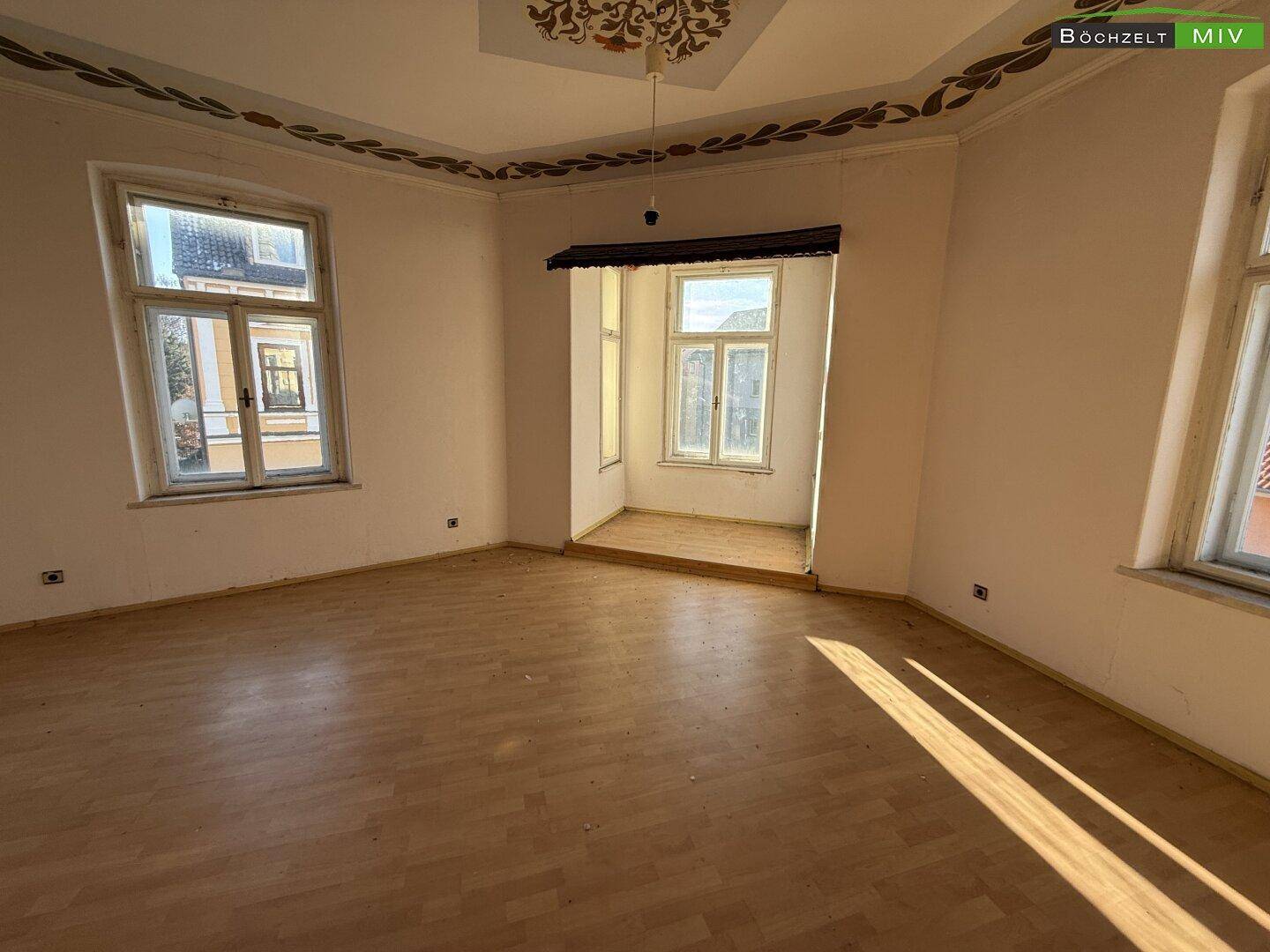 Geräumiger Raum mit Laminatboden, Stuckdecke und einem Erkerfenster, das viel Licht spendet.