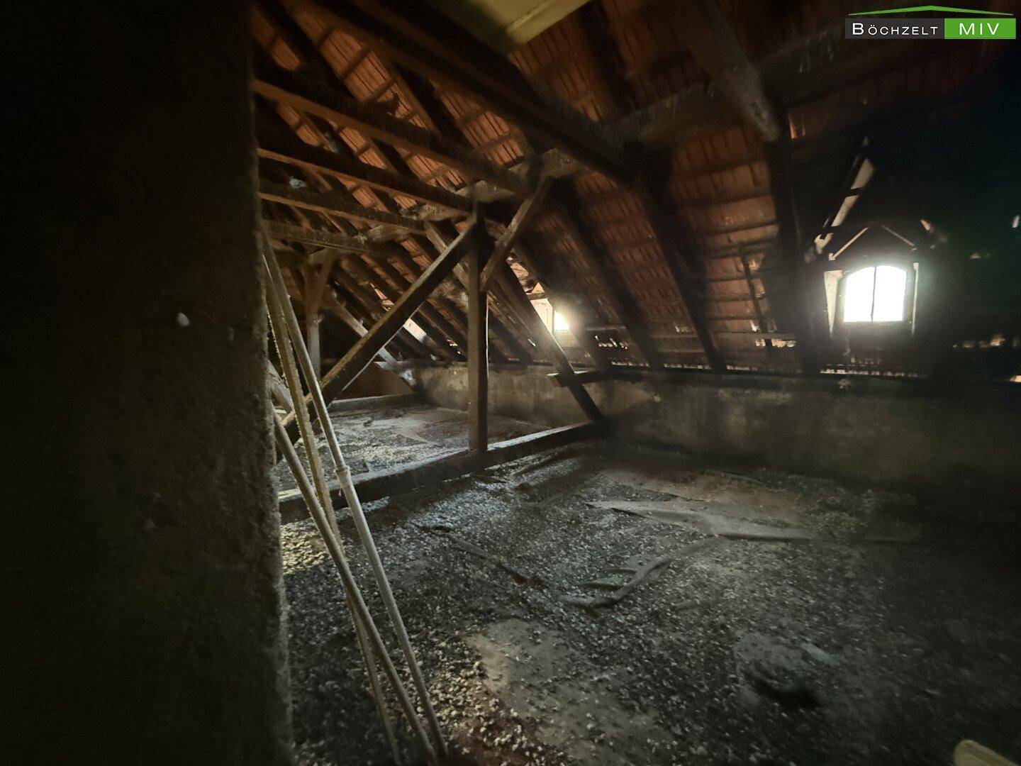 Geräumiger Dachboden mit sichtbaren Holzbalken und einem Fenster, das Licht hereinlässt.