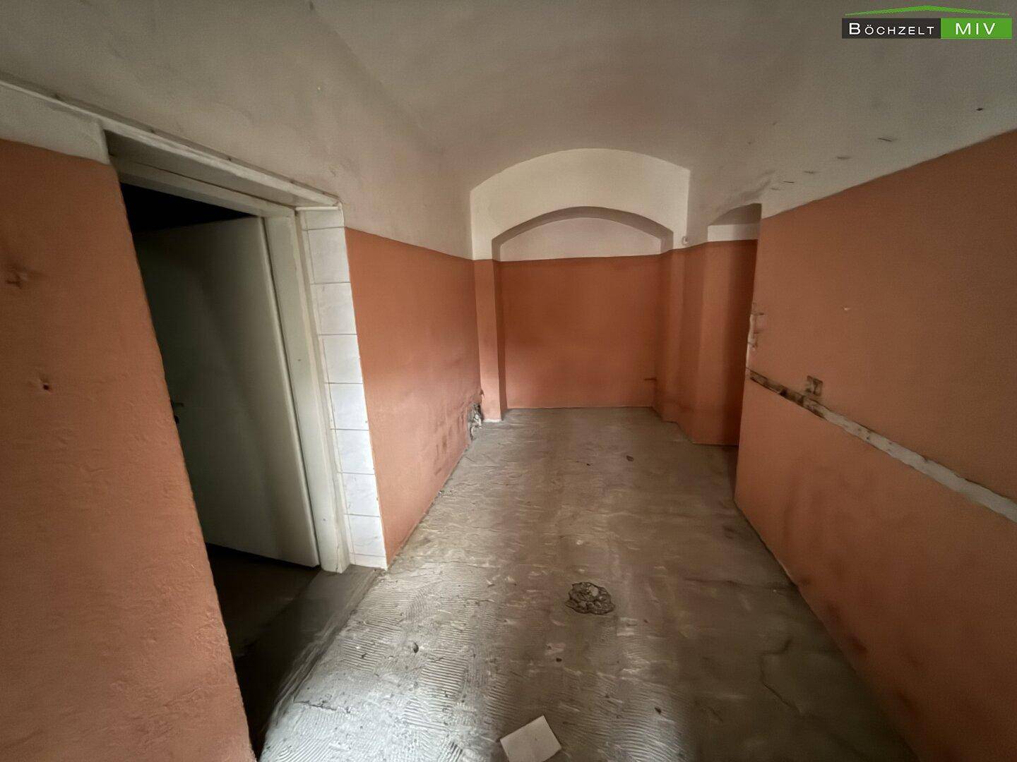 Schmaler Raum mit orangefarbenen Wänden und einem einfachen Boden, der auf Renovierung wartet.