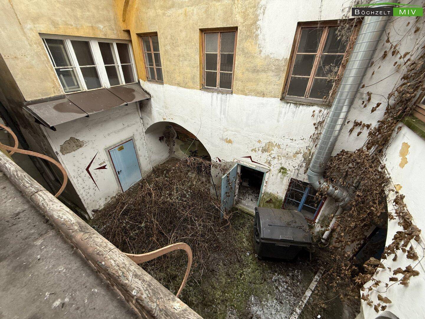 Vogelperspektive auf einen vernachlässigten Innenhof mit viel Wildwuchs und alten Gebäudestrukturen.