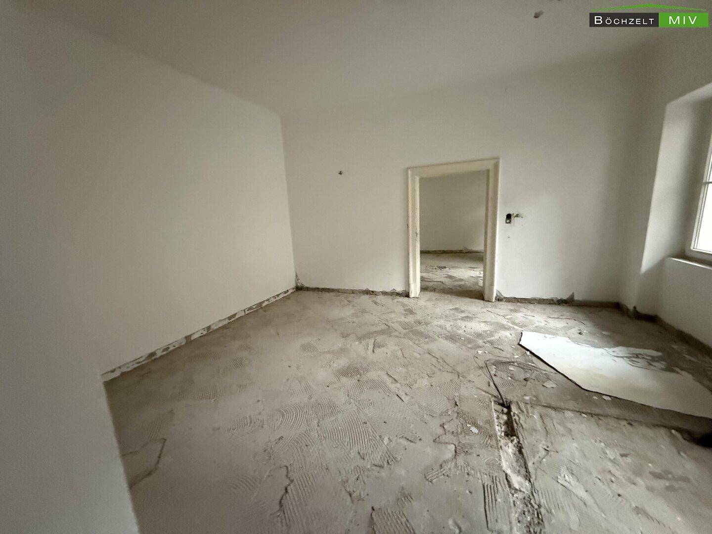Leerer Raum mit weißen Wänden und unfertigem Boden, bereit für die Neugestaltung.
