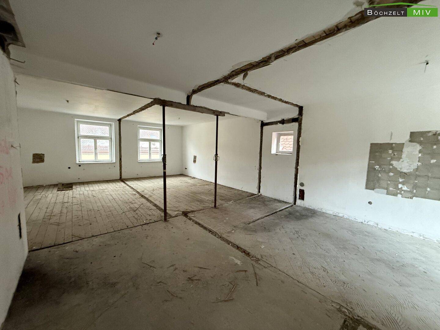 Weitläufiger Raum im Rohbau mit freiliegenden Trägern und unfertigen Böden, der auf Ausbau wartet.