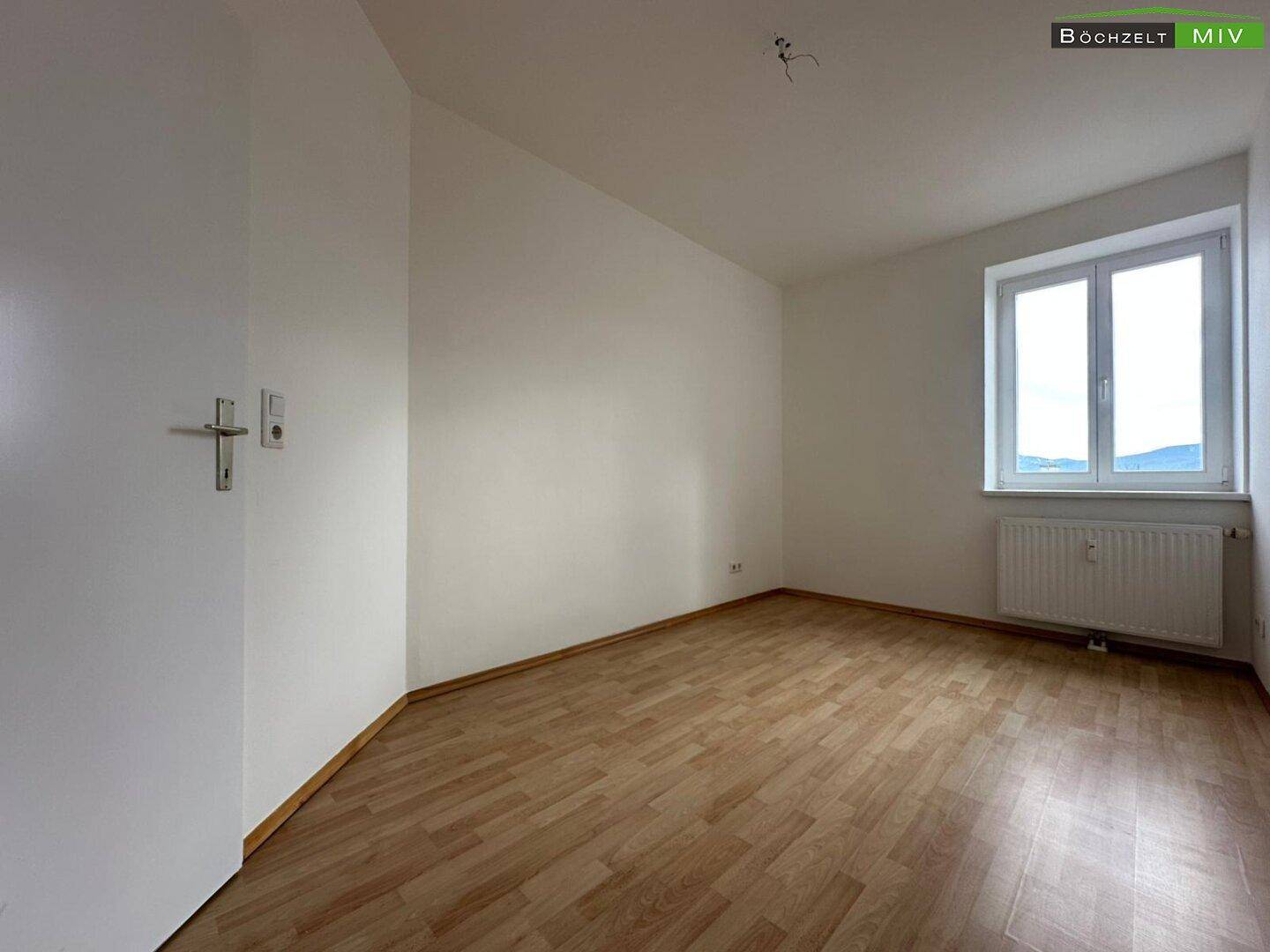 Leeres Zimmer mit Parkettboden, weißen Wänden und Blick auf die Berge.