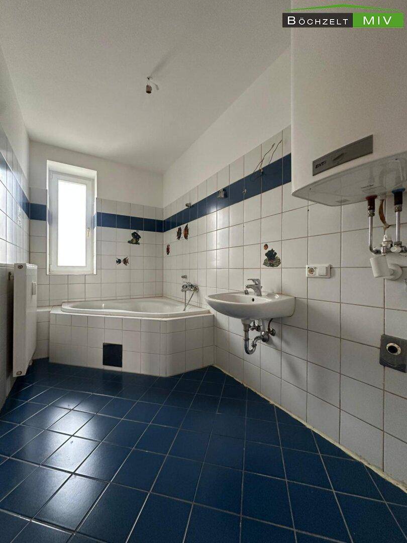 Geräumiges Badezimmer mit blauen Bodenfliesen, weiß-blauen Wandfliesen und Eckbadewanne.