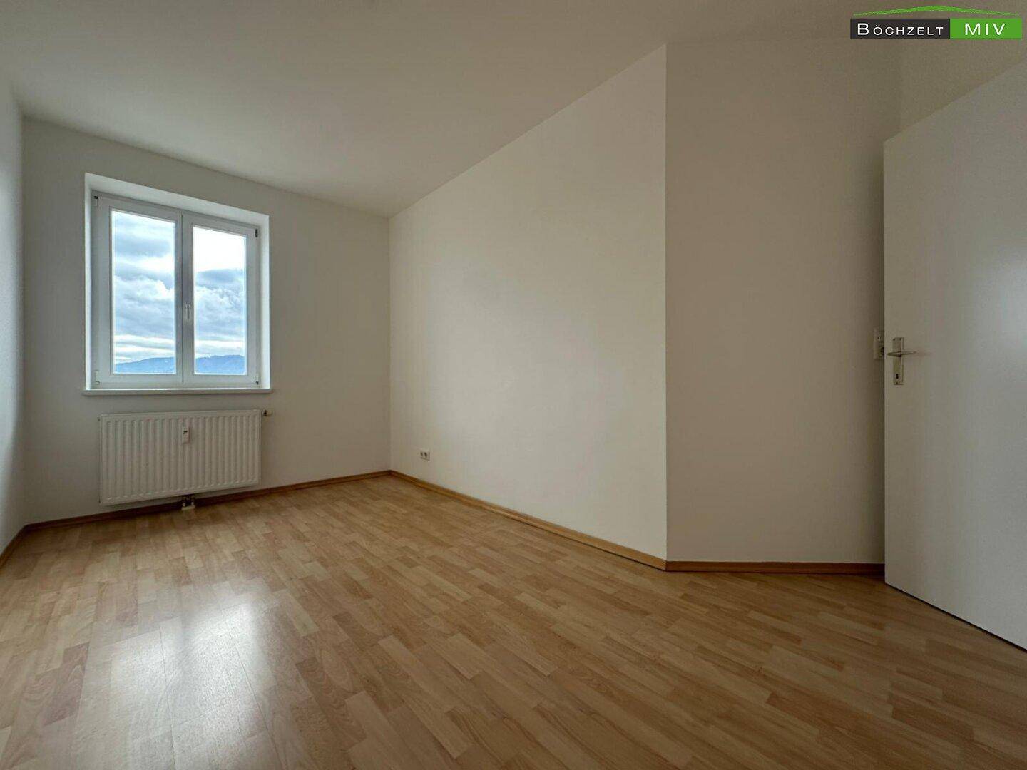 Helles Schlafzimmer mit Parkettboden, weißen Wänden und Fenster mit Bergblick.
