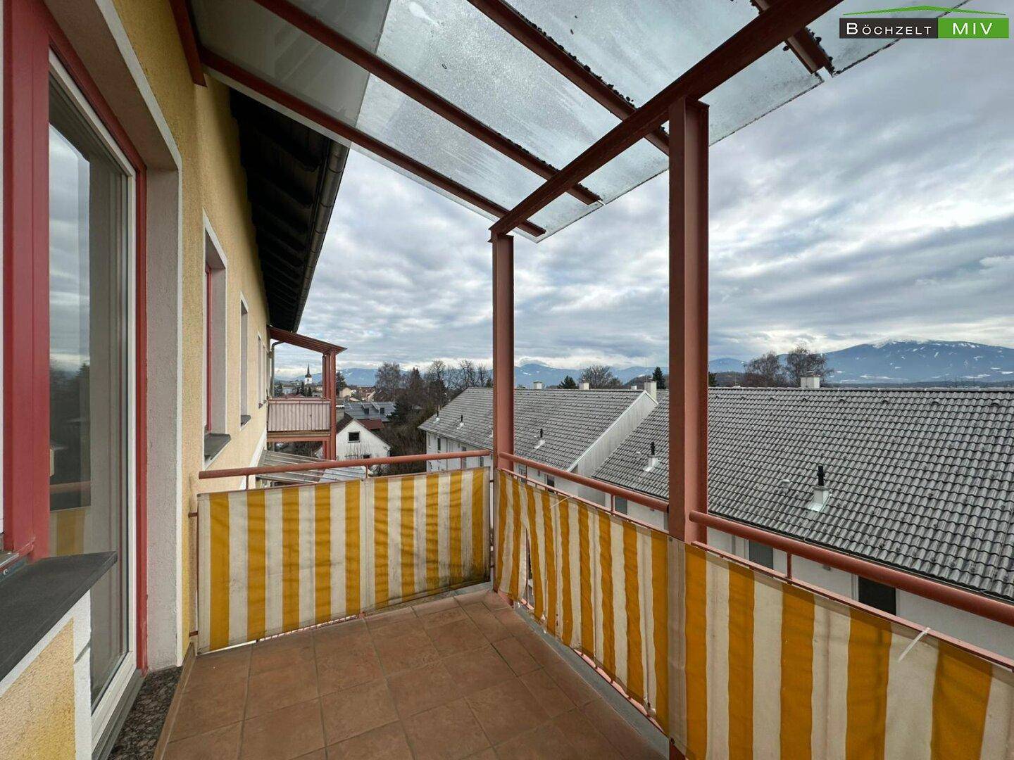 Überdachter Balkon mit gestreiftem Sichtschutz und weitem Blick auf die Berge und Dächer.