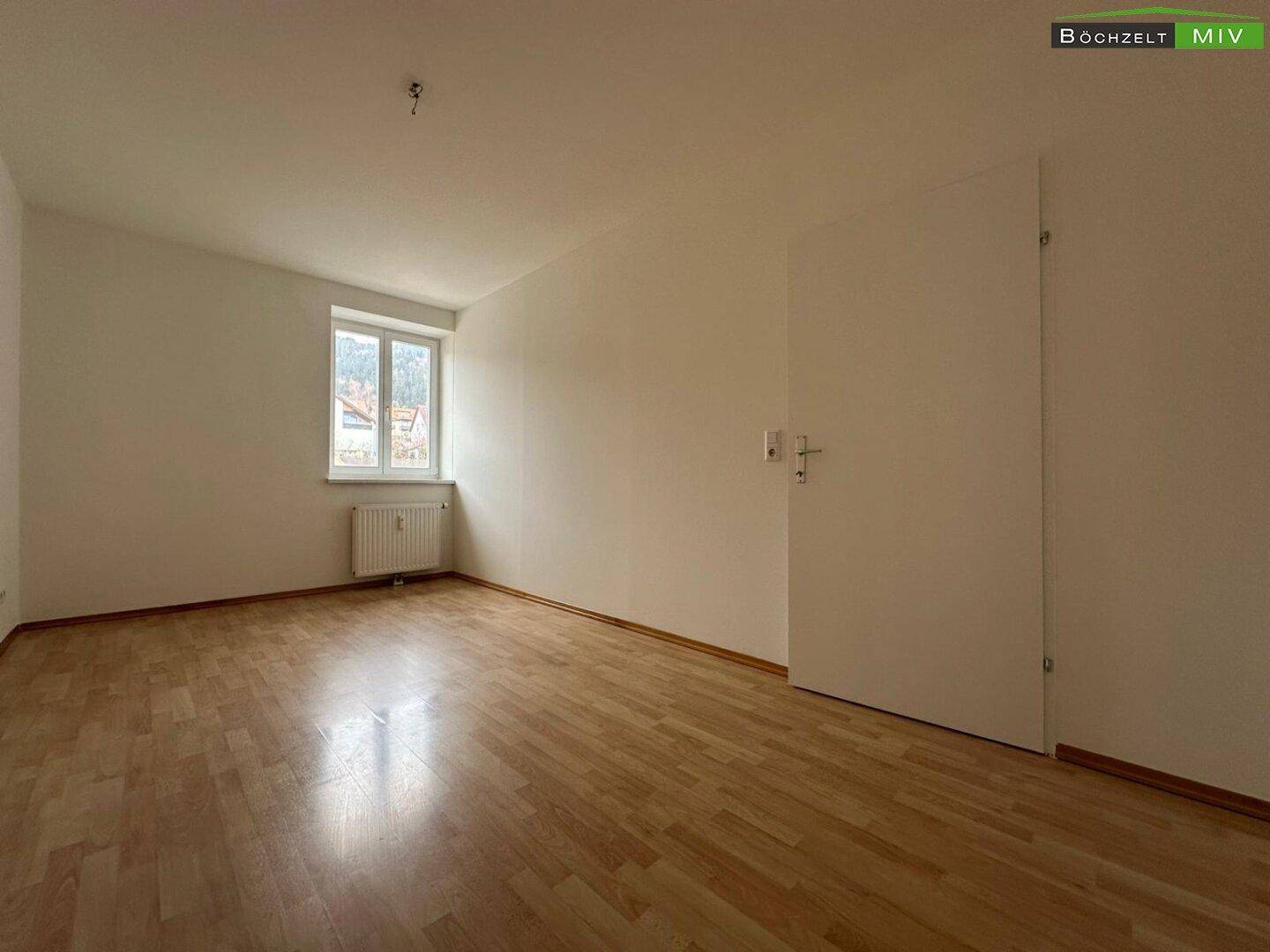 Leeres Zimmer mit Parkettboden, weißen Wänden und Blick auf die Umgebung.