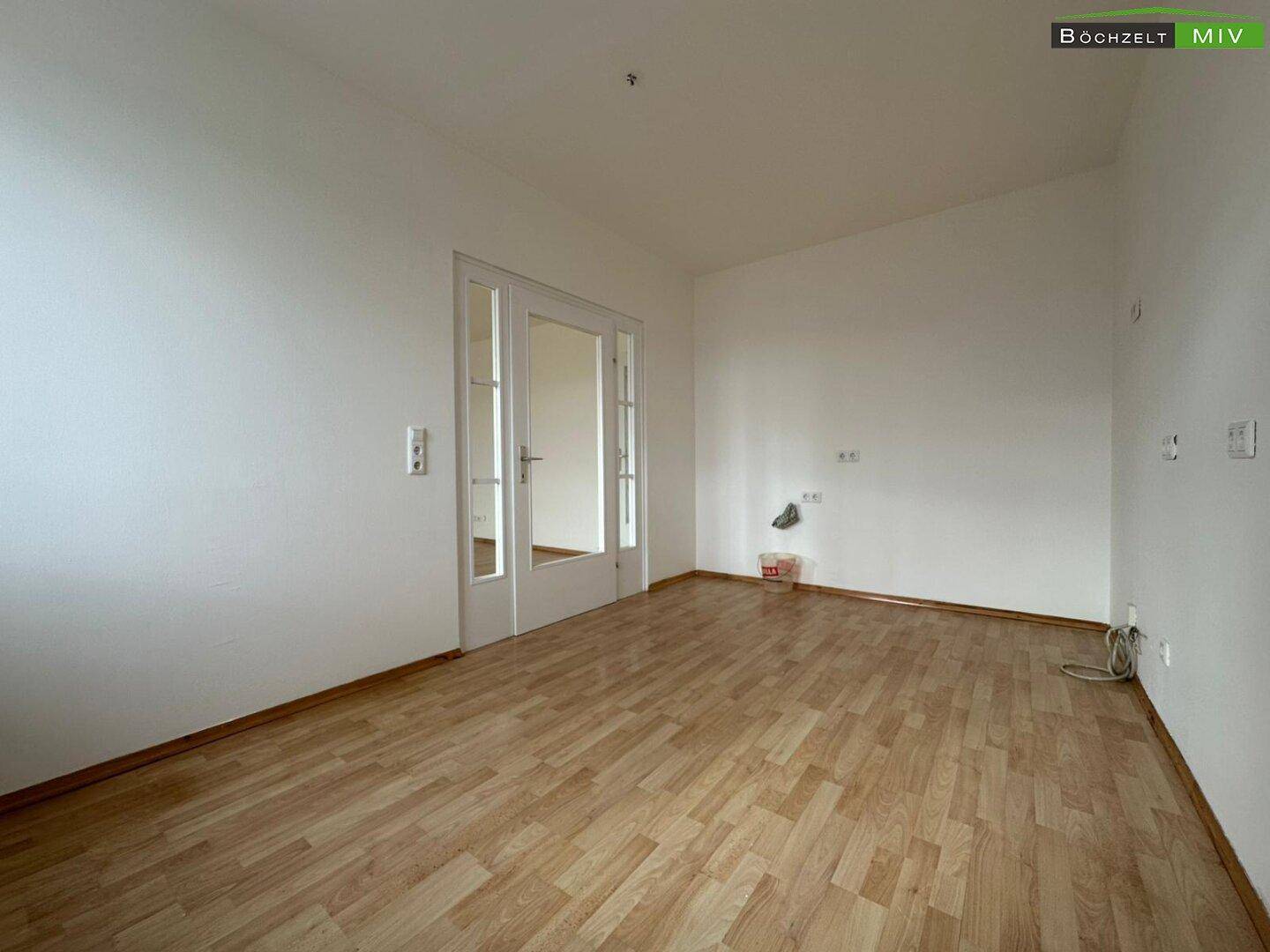 Heller Raum mit Parkettboden, weißen Wänden und einer Glastür.