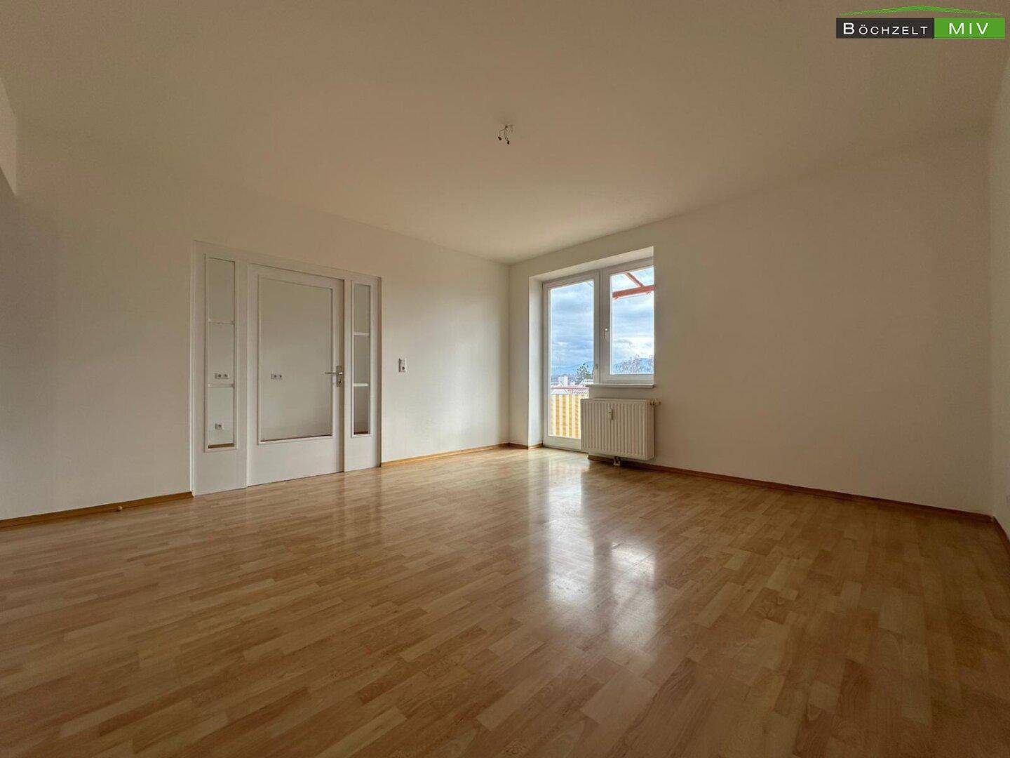 Heller Wohnraum mit Parkettboden, weißen Wänden und direktem Zugang zum Balkon mit Bergblick.