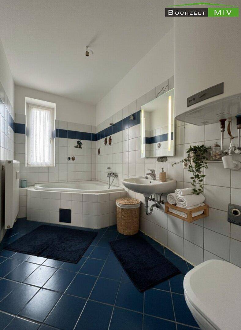 Badezimmer mit blauen Fliesen, Eckbadewanne, Waschbecken und Fenster für Tageslicht.