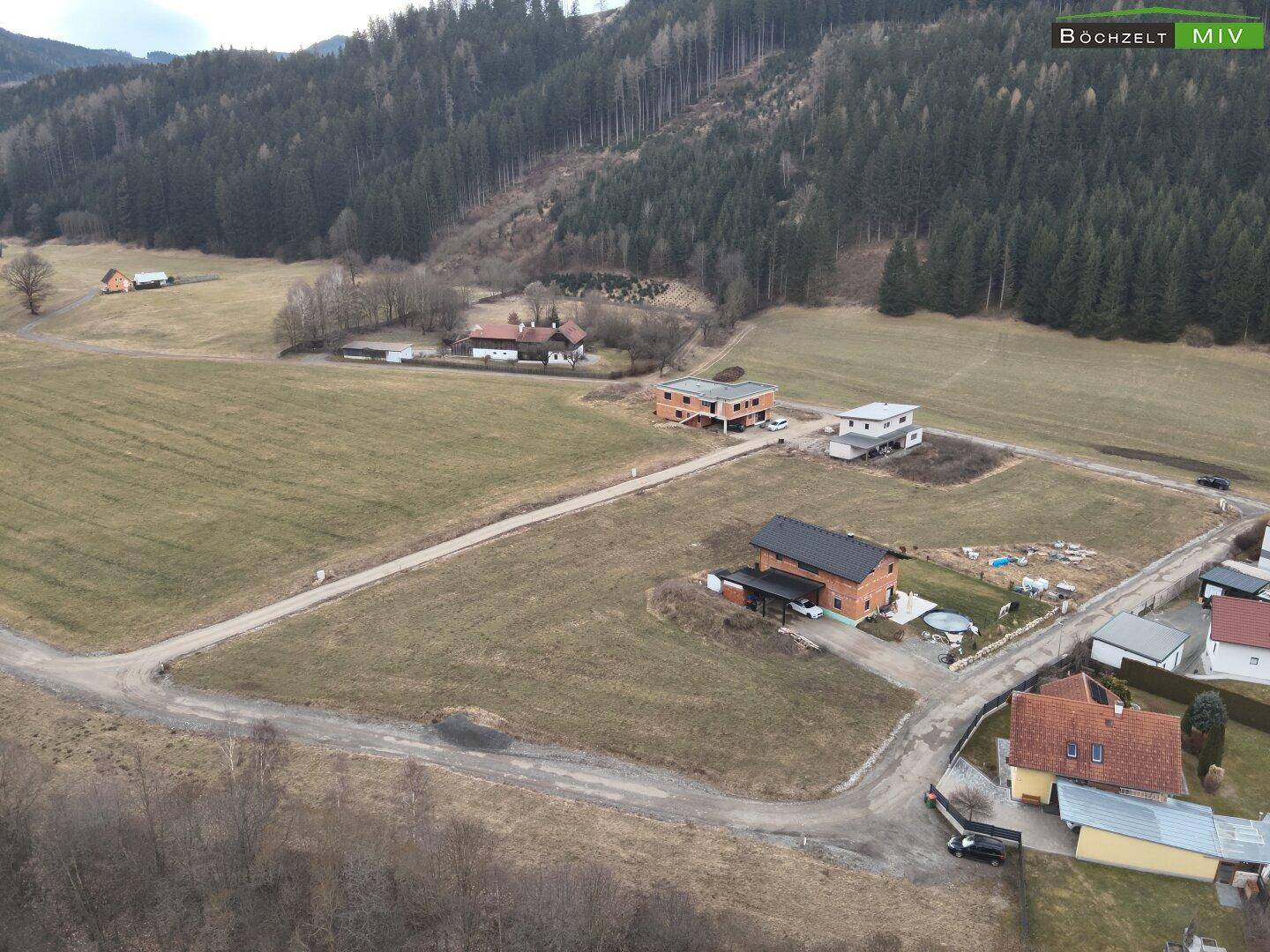 Panoramablick auf ein Wohngebiet mit Neubauten, umgeben von Feldern und bewaldeten Hügeln.