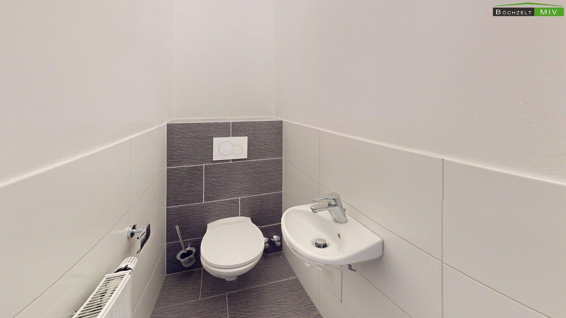 Modernes Gäste-WC mit Wand-WC, kleinem Waschbecken und grauen Fliesen.