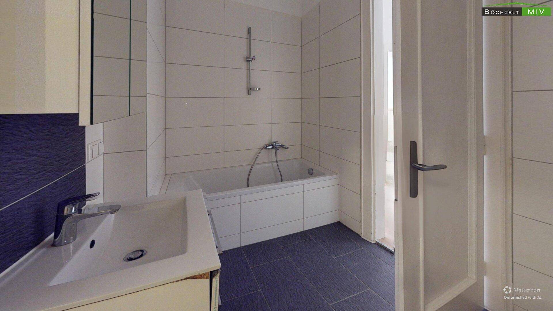 Badezimmer mit Badewanne, Waschbecken und dunklen Bodenfliesen.